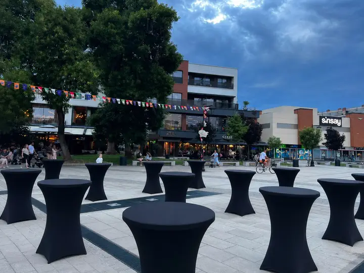 Barski stolovi sa crnim navlakama postavljeni na gradskom trgu
