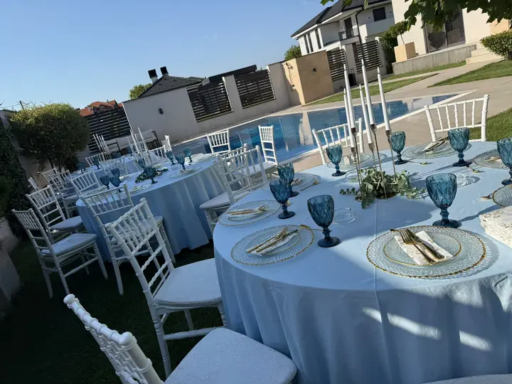 Okrugli stolovi sa belim chiavari stolicama u dvorištu sa bazenom